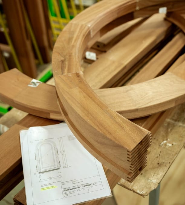 Gebogen houten toogdelen op de werkbank naast de werktekening