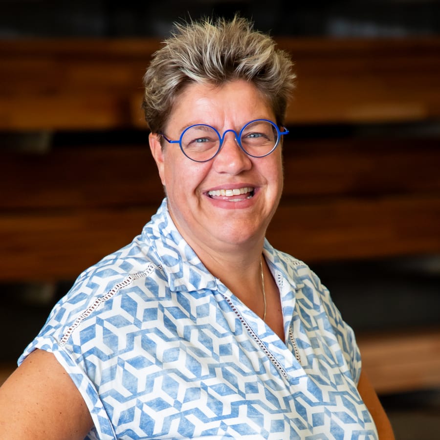 Ria, lachend met blauwe bril in de fabriekshal