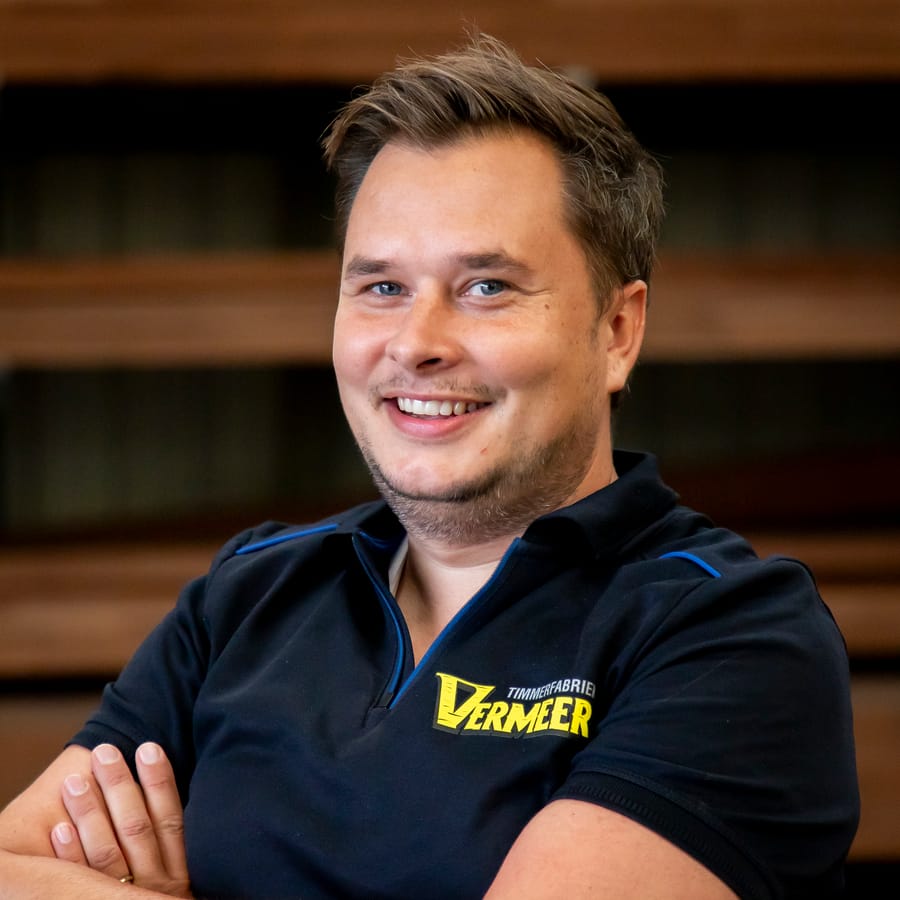Wessel, lachend met de armen over elkaar voor de houtopslag